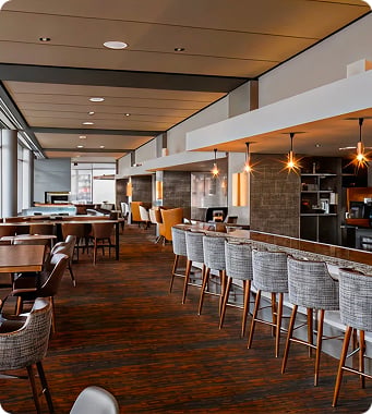 Modern restaurant interior with warm lighting, features high stools at a bar, wooden floors, and cozy seating. Inviting and stylish ambiance. Modern restaurant interior with warm lighting, features high stools at a bar, wooden floors, and cozy seating. Inviting and stylish ambiance.